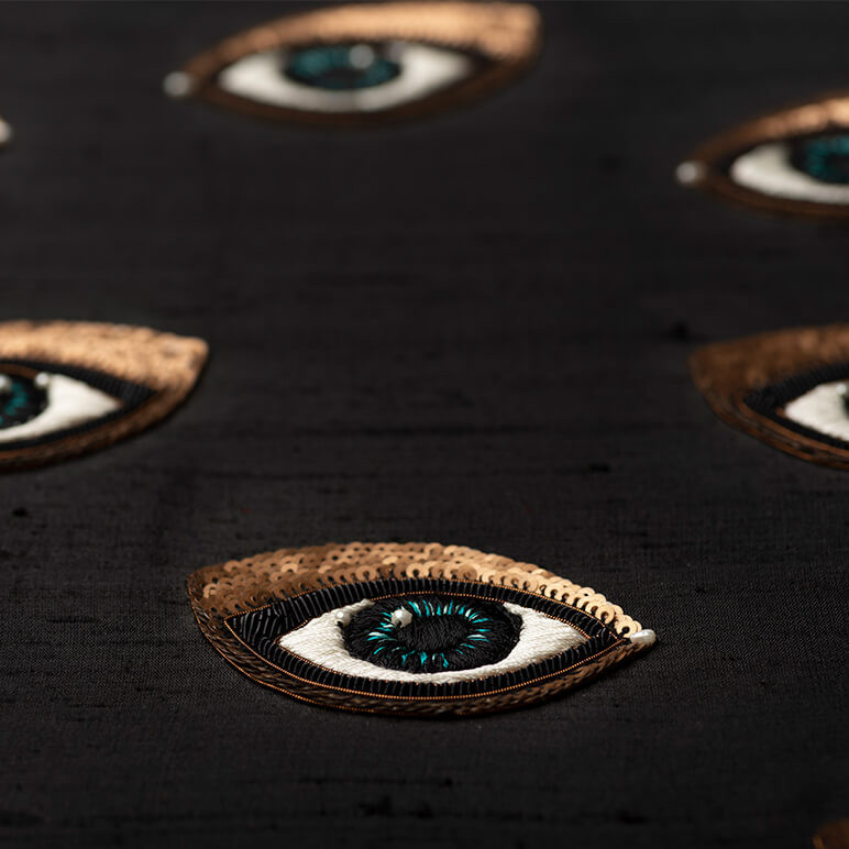 close-up embroidery detail of a sequined eye over a black silk background