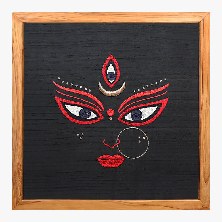 Product feature image showcasing a Goddess Durga textile art hand-embroidered in white, red and gold over a black raw silk background, framed in wood