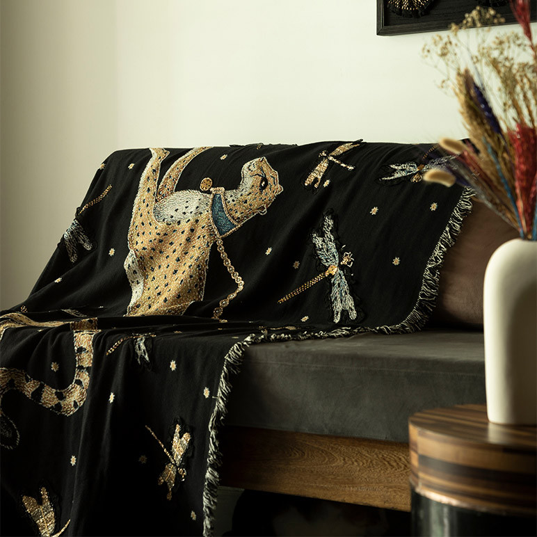 black colored woven throw blanket with a cheetak and many dragonflies seen stylistically laid on the edge of a couch