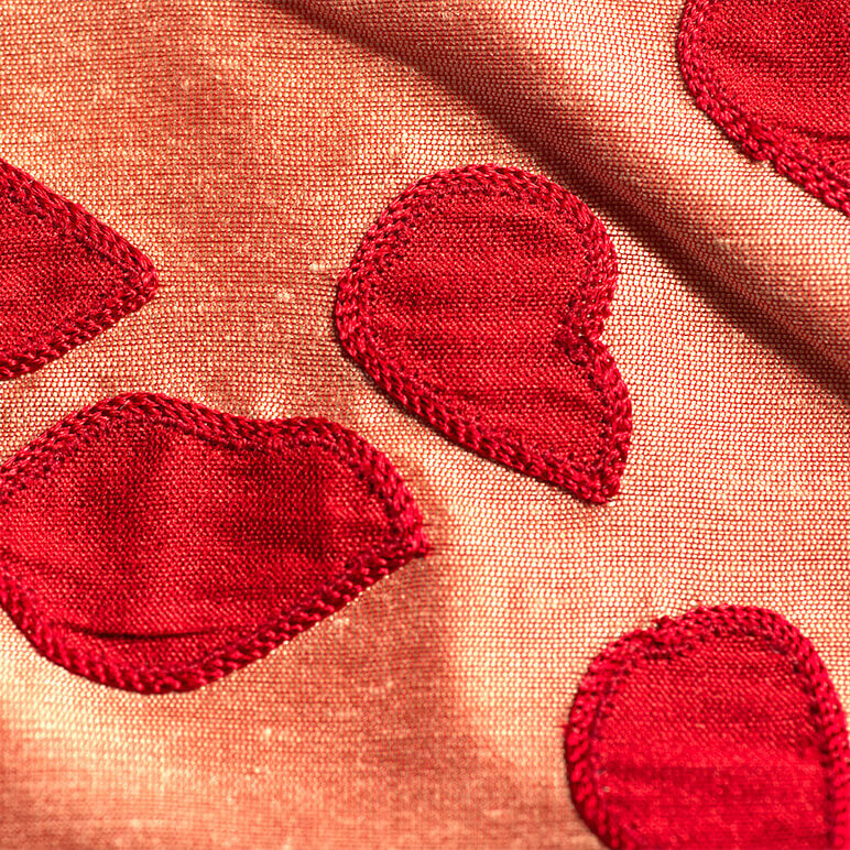 close-up view of an embroidered patchwork tapestry in jewel tones of pink and red