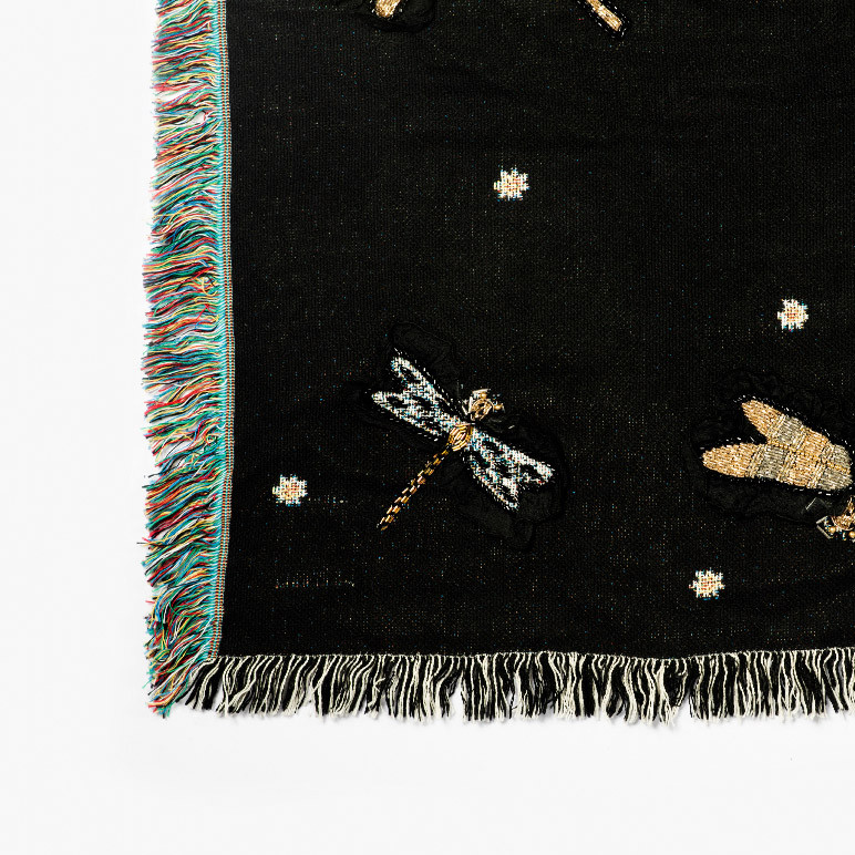 fringe tassel detail of a corner of a black woven wall hanging that is also a throw blanket
