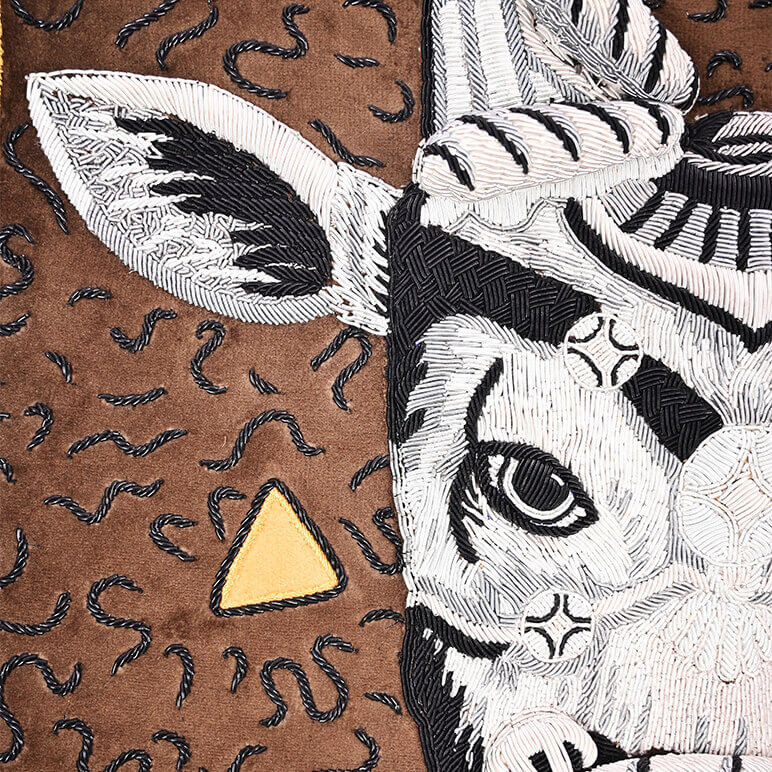 closeup view of the metallic embroidery done to sculpt an Indian bull's head over a brown suede fabric background. Half the head is seen along with squiggly metallic lines that artistically fill parts of the rest of the background