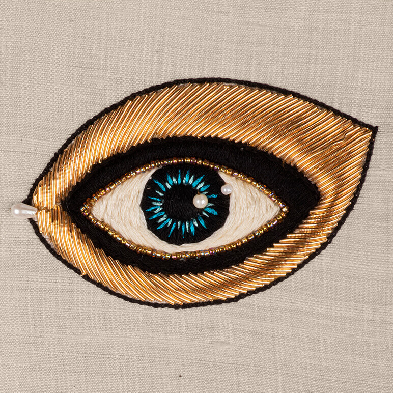 close-up view of an embroidered blue eye done using metallic and silk thread 