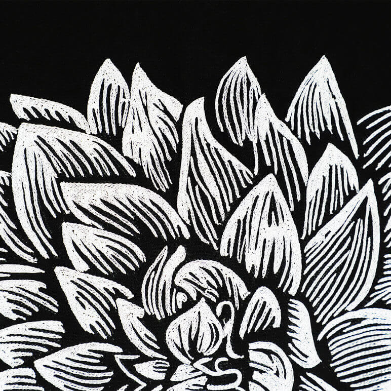 close-up view of chainstitch embroidery in white, forming the petals of a large dahlia flower over a black cotton background