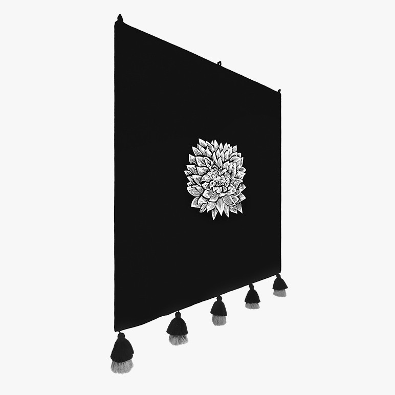 side angle view of a monochrome artwork in the form of a black tapestry with a white embroidered flower at the center
