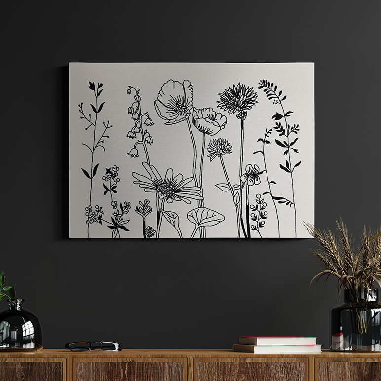 Staged image of a modern minimalistic floral wall art in off-white and black, seen displayed over a dark colored wall