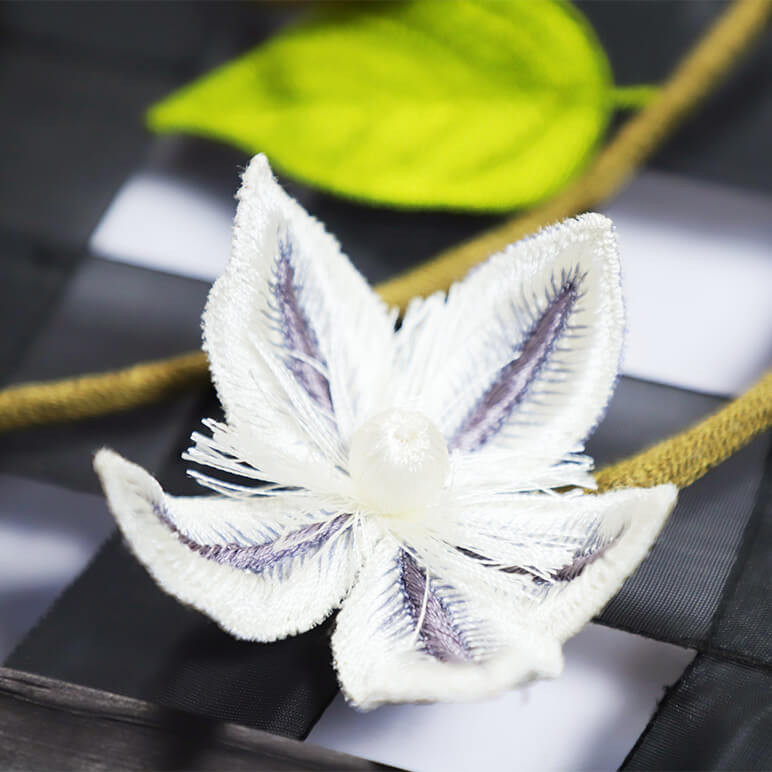 closeup view of an embroidered white flower over a floral vine