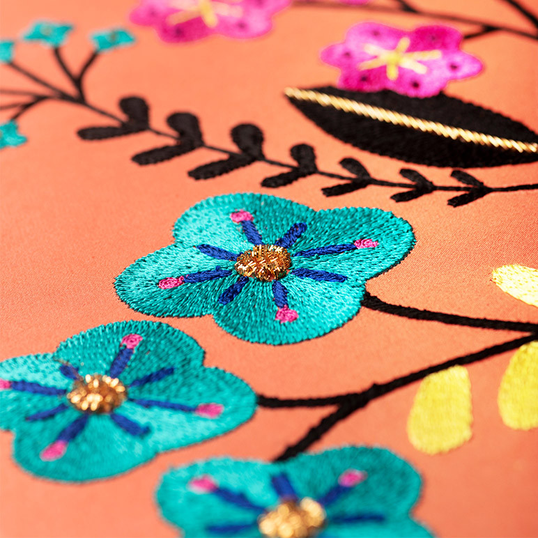 closeup detail of embroidered blue flowers on an orange cotton background