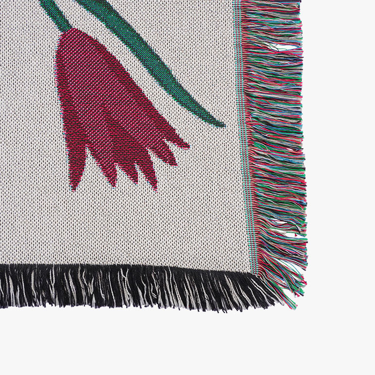 Corner of a jacquard woven throw blanket with a multicolor fringe and a red tulip on it