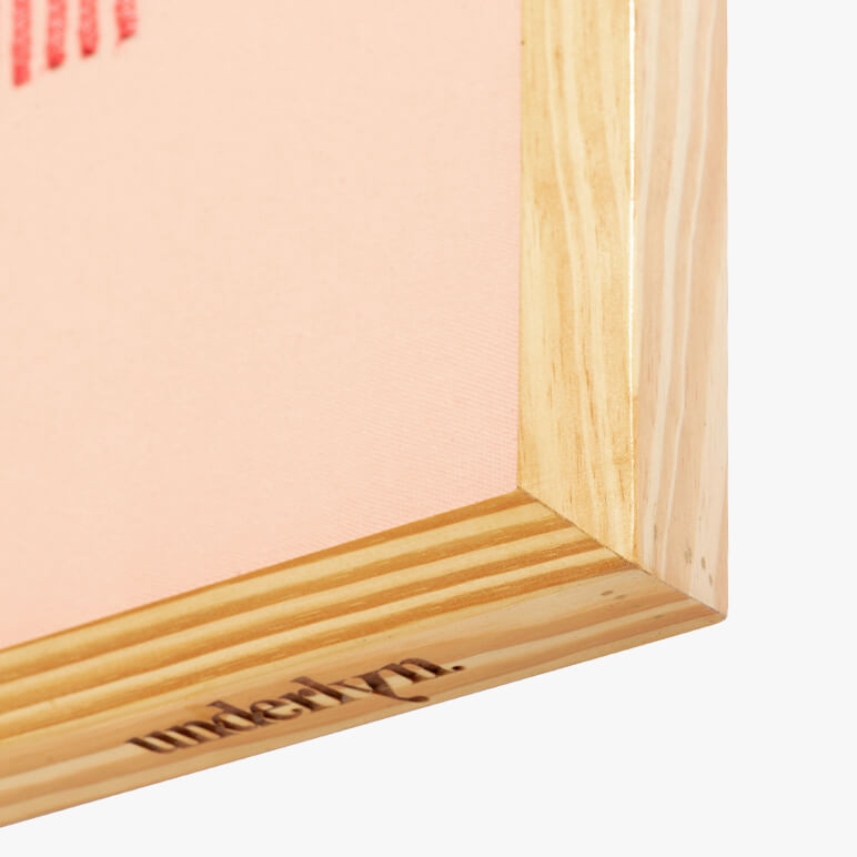 closeup view of an etched corner of a wooden frame holding a pink wall artwork