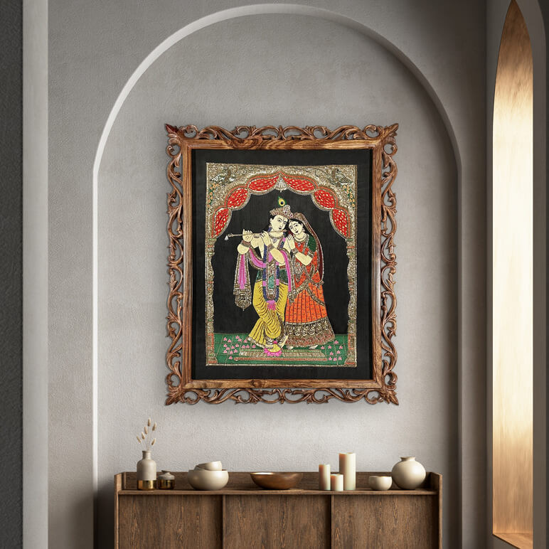 Staged view of a framed textile artwork showcasing Lord Krishna and Radha, framed in a dark ornate hand carved frame