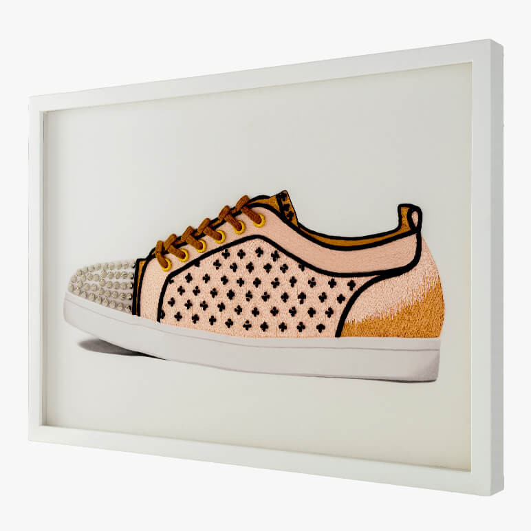 side angle view of a textile wall art featuring a hand-embroidered shoe framed in a white gallery frame