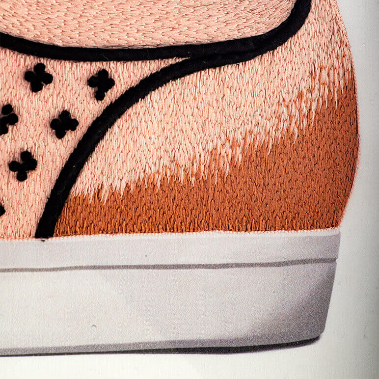 closeup view of the back part of an embroidered shoe done in nude, brown and black colored thread