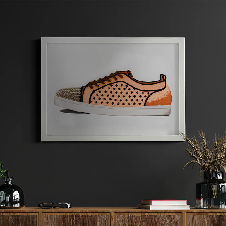 framed shoe textile wall art in peach, brown and black, seen displayed in a dark room