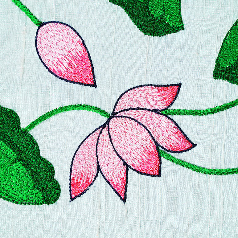 Detailed view of the embroidered lotus flowers in pink with green stalks, seen over a pastel blue silk background