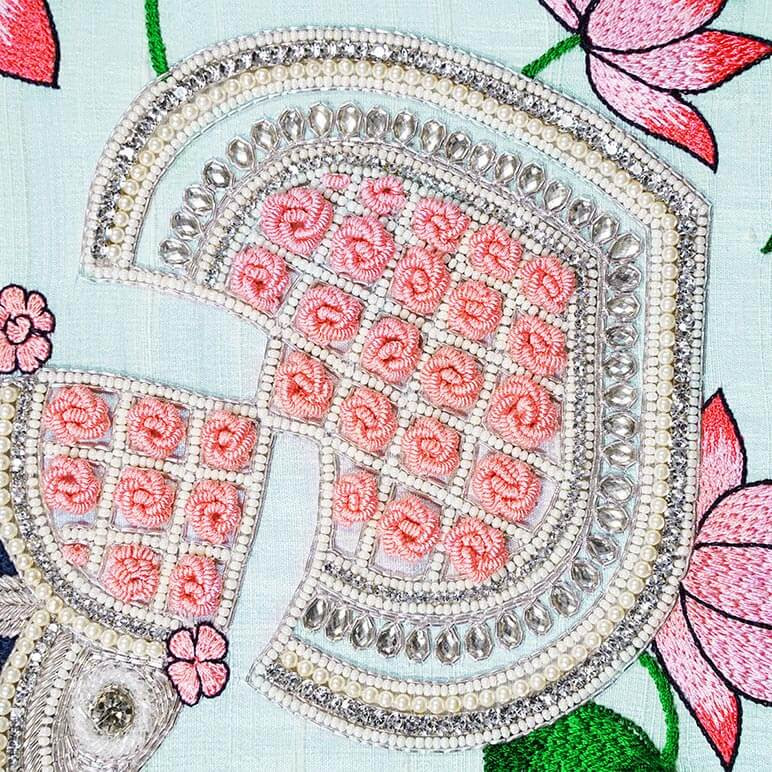 Close up view of zardozi and silk thread embroidery done in pink and silver colors over a pastel blue background