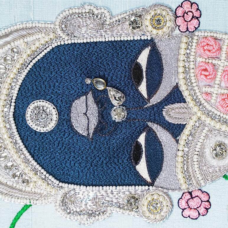 Detailed view of the embroidery of Shrinathji in blue, pink and silver colors over a pastel blue fabric