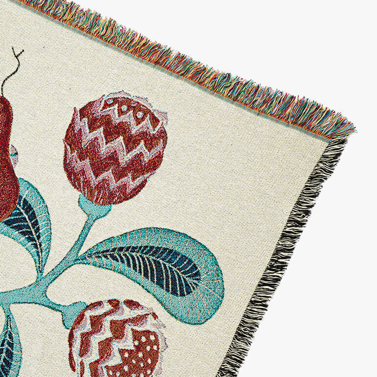 corner view of a woven throw blanket showing a red snake head and a large red flower over an off-white background