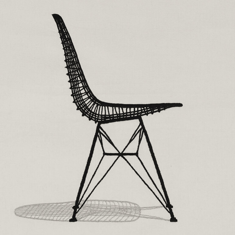 close-up view of an embroidered Eames wire chair in black at the center of a beige colored cotton background