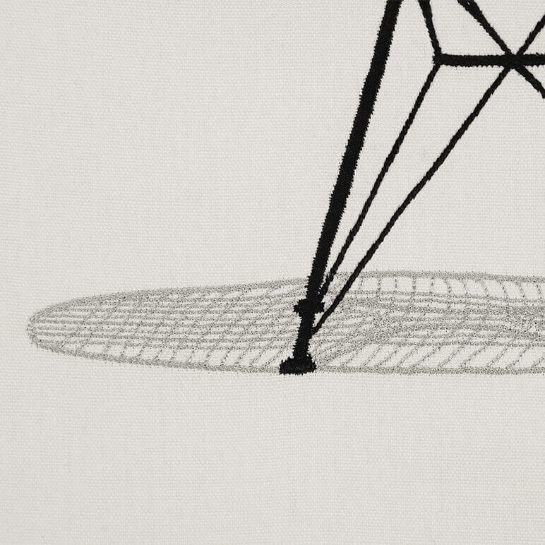 close-up view of the hand-embroidery of a chair's shadow seen over a beige cotton background