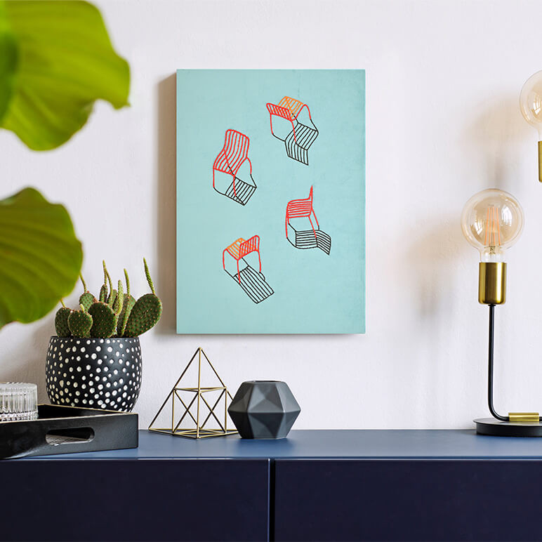 Style shot of a still life artwork featuring a group of red chairs embroidered over a suede blue background, seen displayed over a blue console table in a vignette