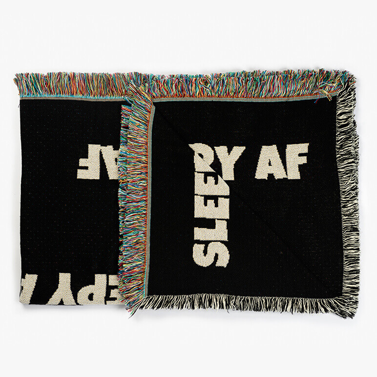folded couch throw blanket in black color with a typographic print on top in white that says sleepy AF