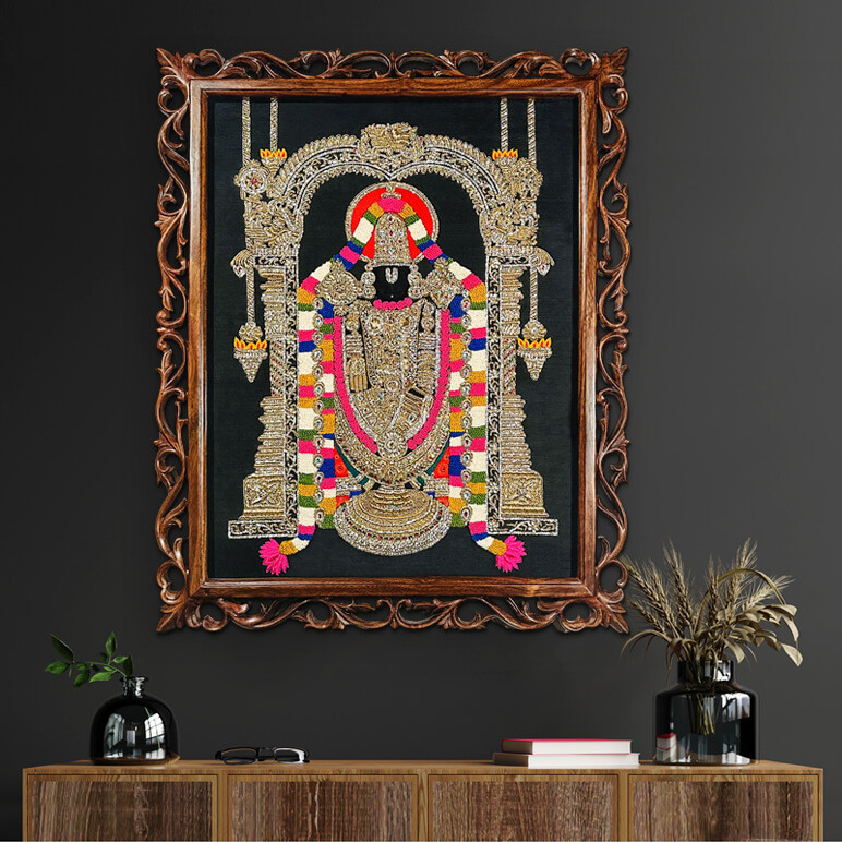 Staged view of Tirupati Balaji artwork, framed in a carved ornate wooden frame, seen displayed over a dark wall above a wooden console table