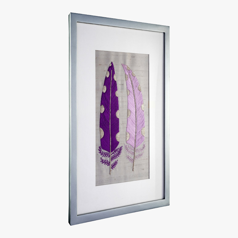 side view of a silver dusted textile art frame featuring two purple embroidered feathers
