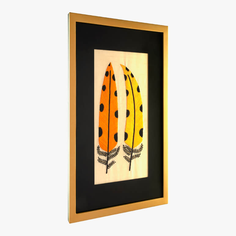side view of a framed modern folk embroidery featuring two yellow feathers with black polka dots