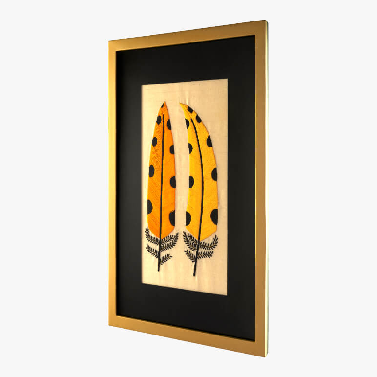 side view of a framed modern embroidery piece with two yellow polka dotted feathers