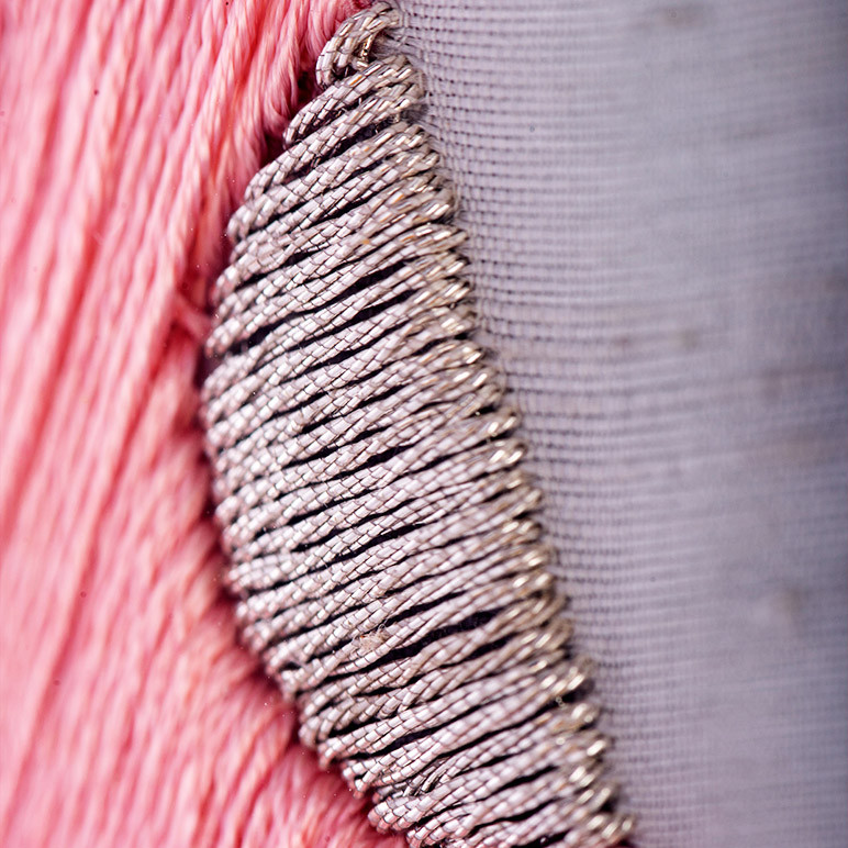 closeup embroidery detail of a part of a pink feather with a grey polka dot