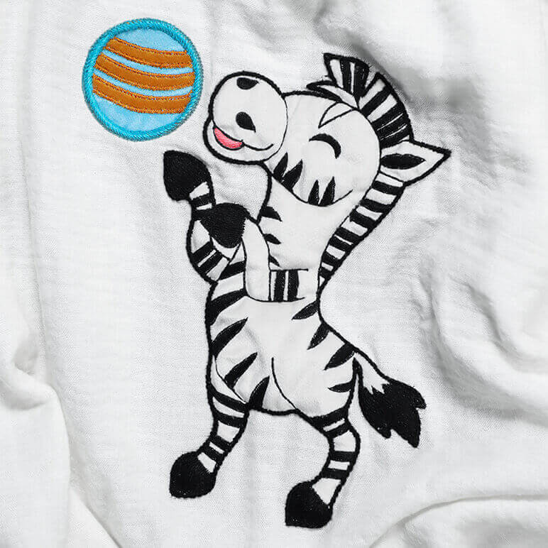 embroidered black and white zebra playing with a blue ball seen over a bamboo cotton fabric background