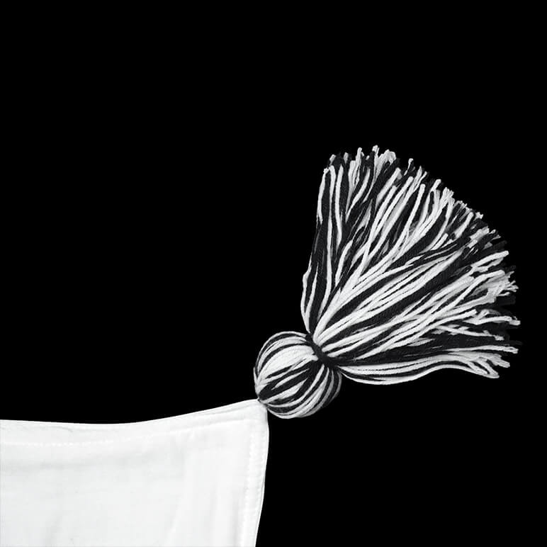 black and white hand-knotted wool tassel at the corner of a white throw blanket seen on a black background